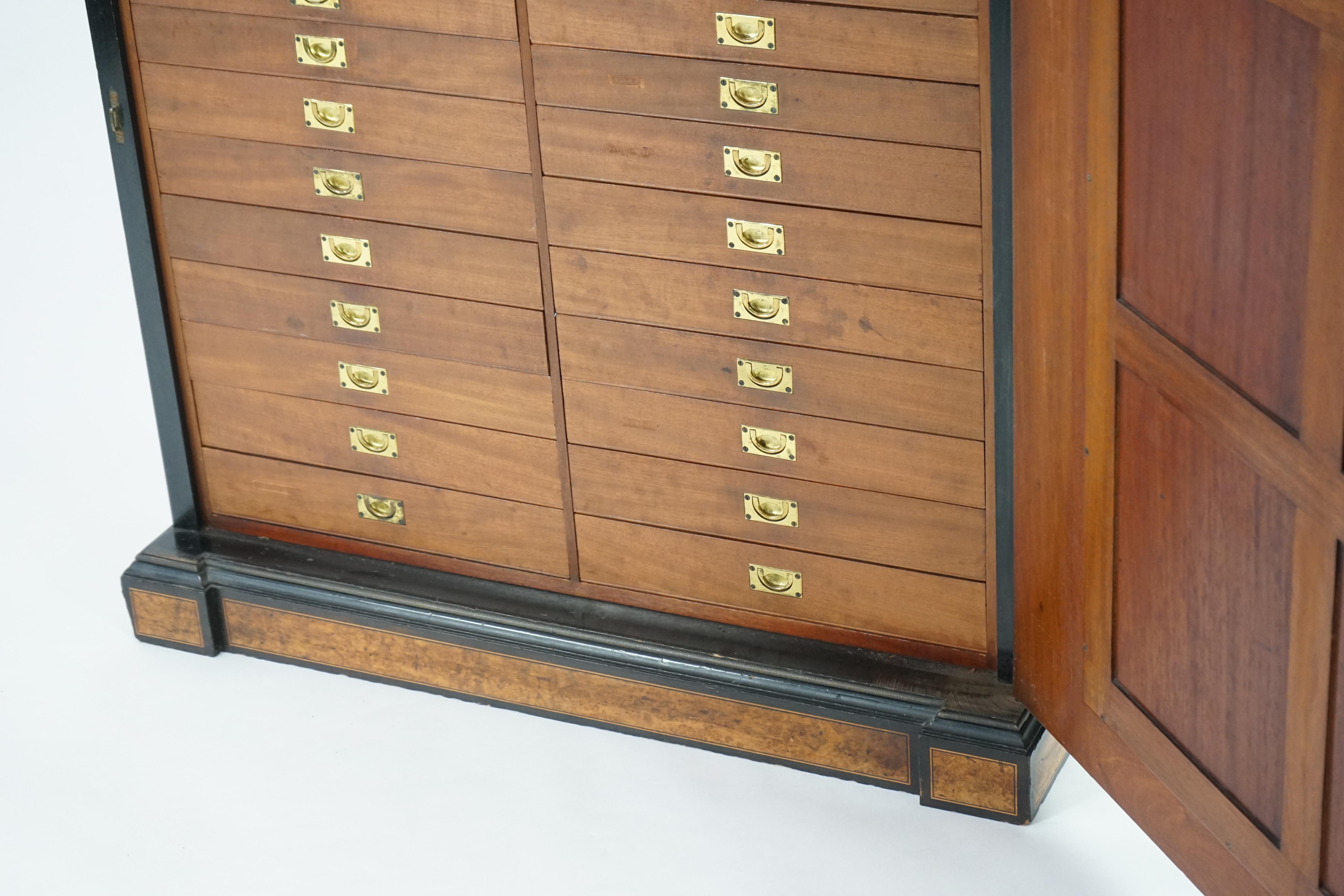 A Victorian ebony banded amboyna wood collector's cabinet, by Holland & Sons, with inverted breakfront top and single mirrored door enclosing four frieze and two banks of thirteen graduated drawers fitted with recessed b